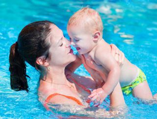 Eine junge Mutter verbringt die Zeit mit Ihrem Baby beim Babyschwimmkurs im Wellenspiel