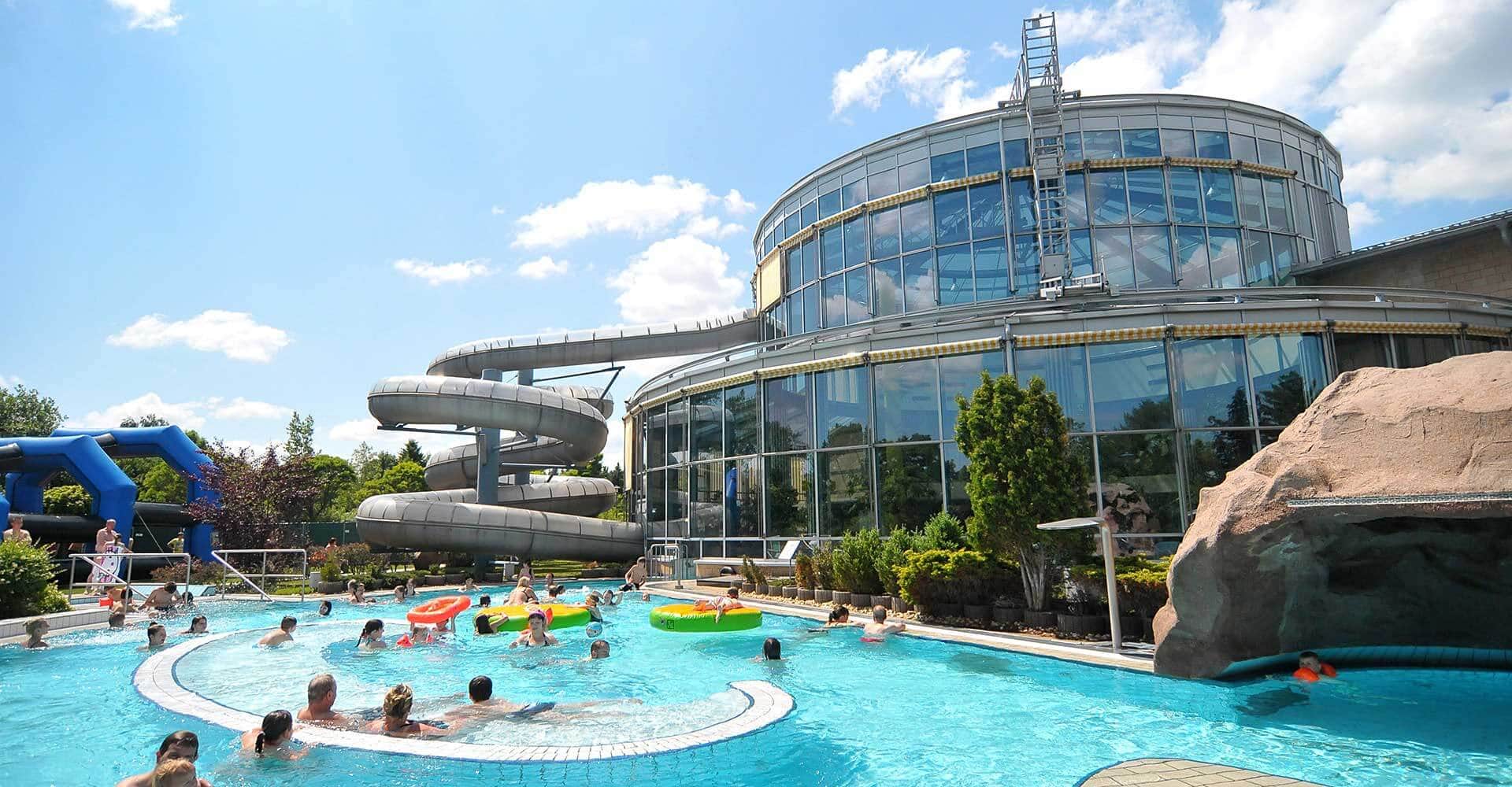 Bei Sonenschein und blauem Himmel genießen Erwachsene und Kinder das kühle Wasser in der Außen-Anlage des Freizeitbades Wellenspiel Meißen. Hinter dem Becken erhebt sich die Riesenrutsche und lädt die Besucher zu Spiel und Spaß ein.